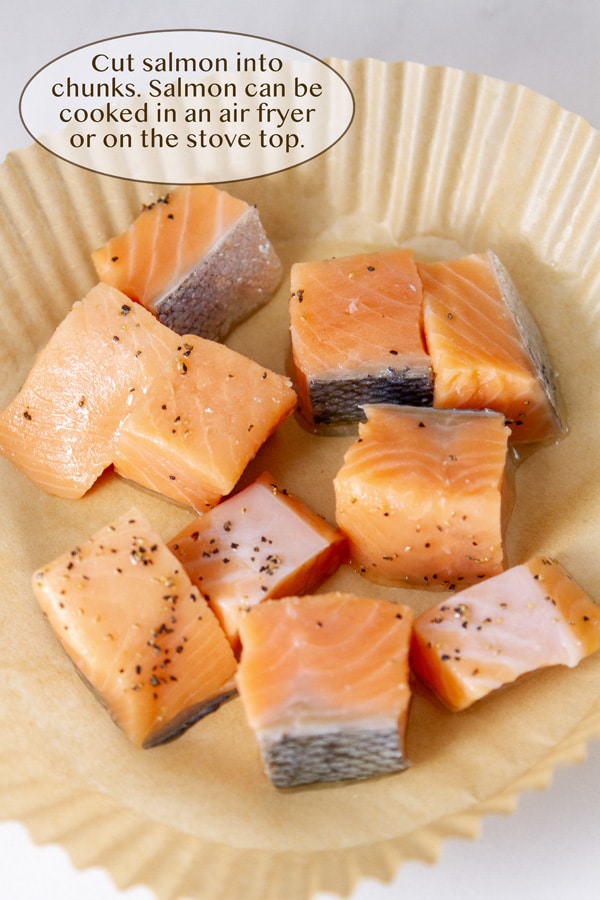 raw salmon cut into small cubes seasoned with pepper in a parchment paper air fryer liner.
