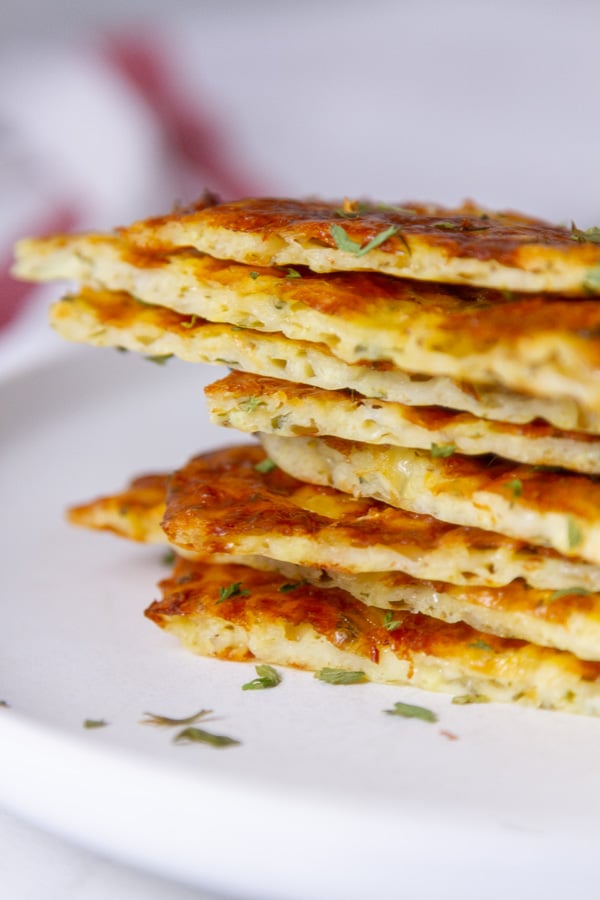a stack of baked cheese sticks on a white plate, a cloth napkin in the background.