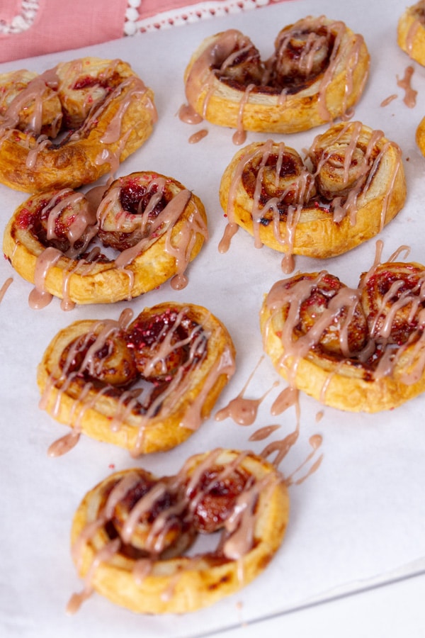 drizzling pink icing over heart shaped cookies on a parchment paper lined cookie sheet.