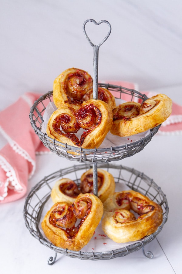Valentine's Day cookies on a wire two tiered serving platter with a pink napkin in the background.