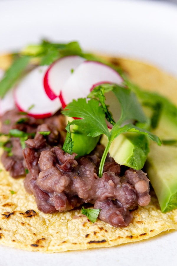 a taco filled with black beans, avocado, cilantro, and radishes.