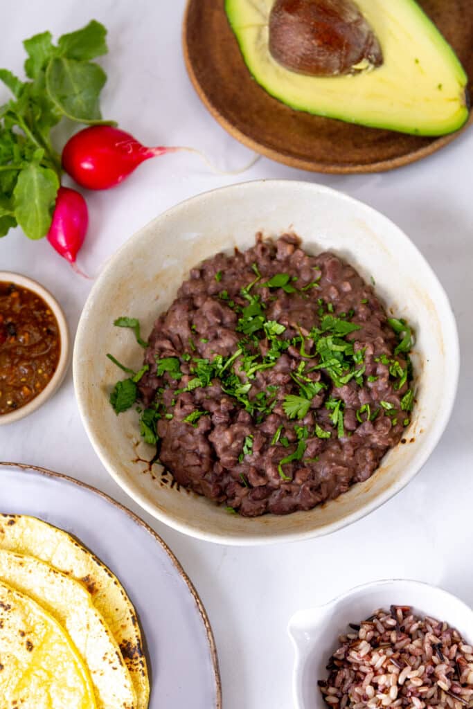 a taco bar with lots of bowls and plates of taco fillings including black beans, rice, avocado, tortillas, salsa, and radishes.
