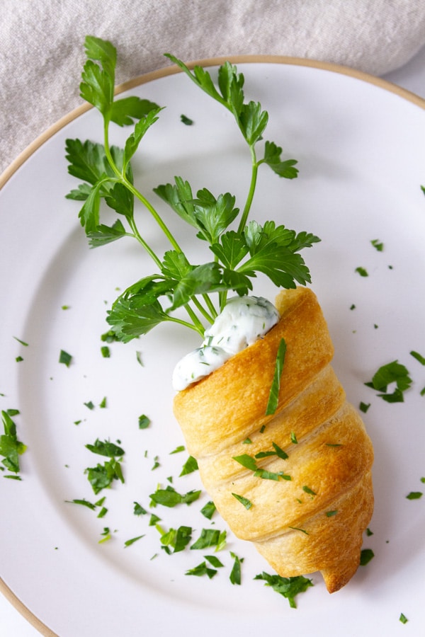 a crescent roll shaped into a carrot on a white plate garnished with chopped parsley.