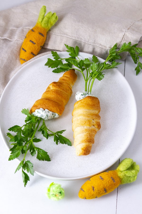 two crescent roll carrots on a white plate with two felt carrots around it.