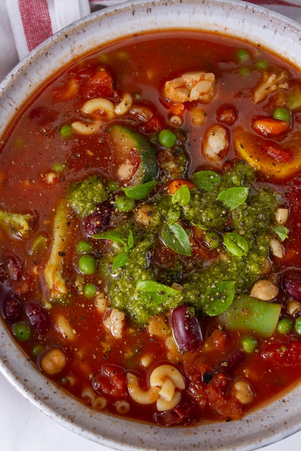 Close up on a bowl of minestrone topped with pesto and basil leaves.
