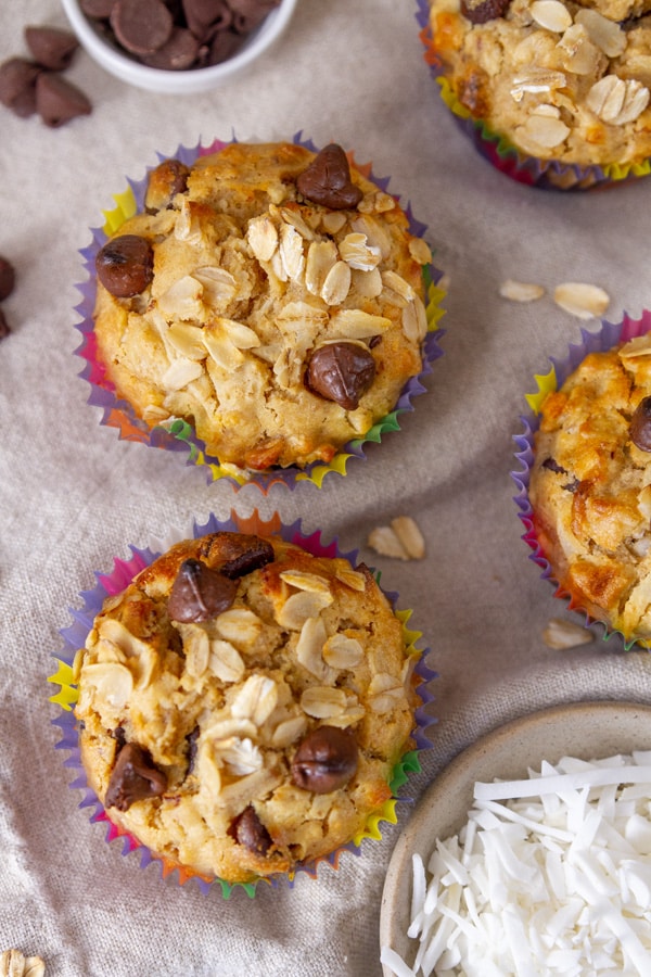 looking down on muffins topped with oats and chocolate chips next to small bowls of ingredients.