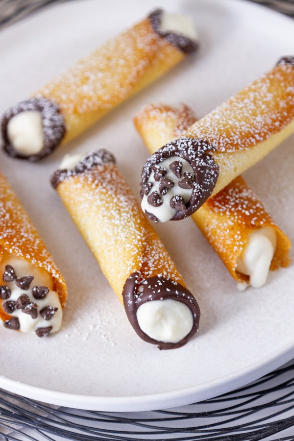 5 cannoli cookies stacked on a plate dusted with powdered sugar.