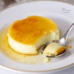 a serving of flan custard with a spoonful next to it on a white plate.