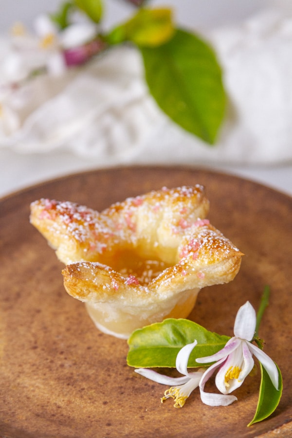 one puff pastry tart on a brown plate with some lemon leaves and flowers around it.