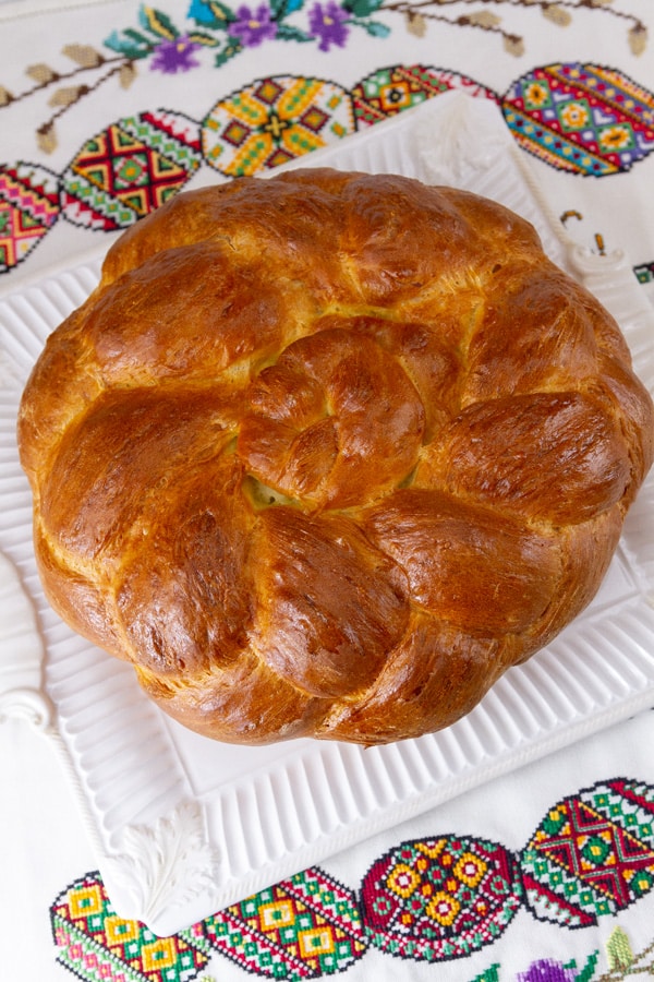looking down on the top of a loaf of bread decorated with braided dough and it's on embroidered egg towels. 