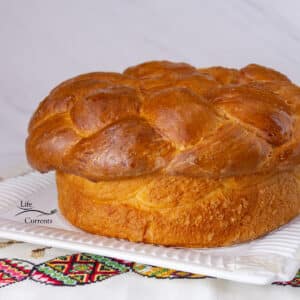 square crop of paska bread on a white platter on embroidered linens.