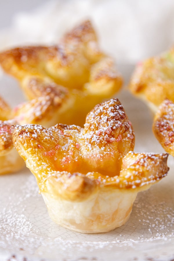 Some puff pastry cups sprinkled with powered sugar on a white plate.