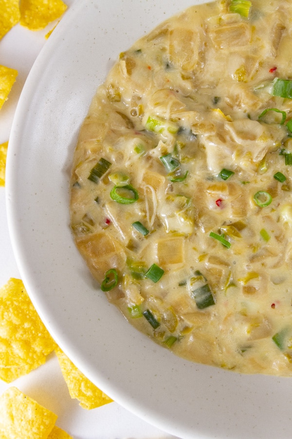 a bowl of melted cheese with veggies in it and chips next to the bowl.