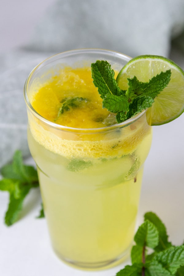 An Imperial pint glass filled with pineapple drink and garnished with mint and fresh lime.