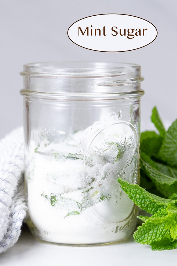 a mason jar filled with mint sugar some sprigs of mint around it and a towel behind it.