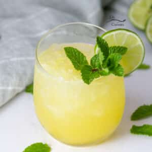 square crop of a glass of pineapple drink garnished with mint and lime.