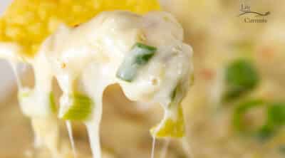 square crop of a tortilla chip dipped into melted cheese dip.