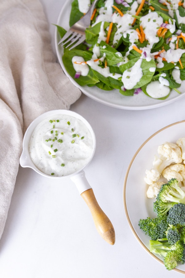 a salad in the upper right a plate of veggies in the lower right and a bowl of ranch dressing for dipping in the middle.