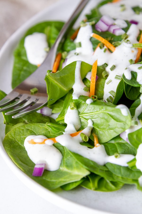 a spinach salad with cottage cheese ranch dressing on it.