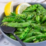 square crop of pes in pods tossed in herbs in a blue bowl with a spoon and lemon wedges.