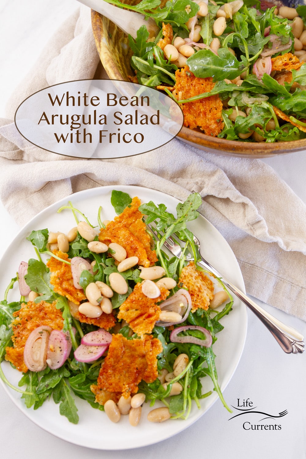 White Bean Arugula Salad with Frico on a white serving plate next to the serving bowl with a cloth napkin in between.