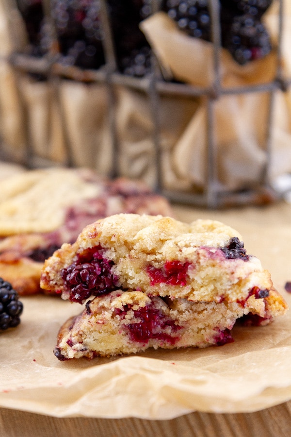 a blackberry cookie cut in half so you can see the inside on a brown piece of parchment paper next to a wire basket of berries.