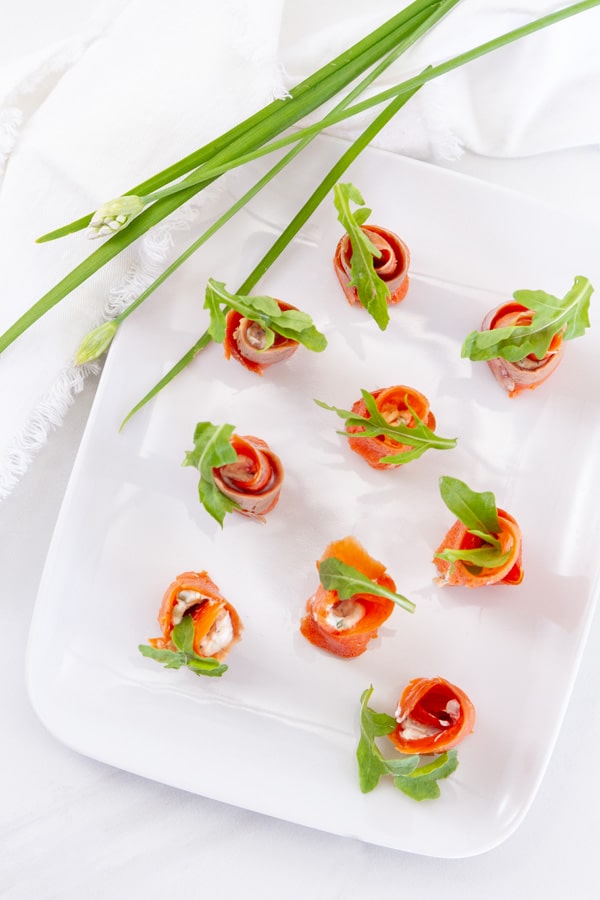 smoked salmon rolls on a white plate with chives and a white cloth napkin next to the plate.