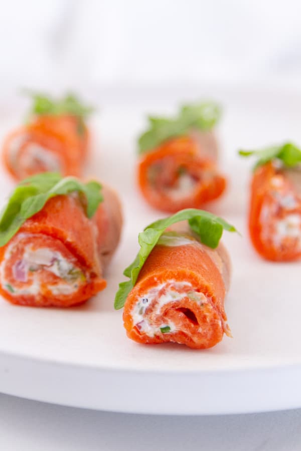 smoked salmon rolls on their side so you can see the cream cheese filling and they are topped with an arugula leaf.