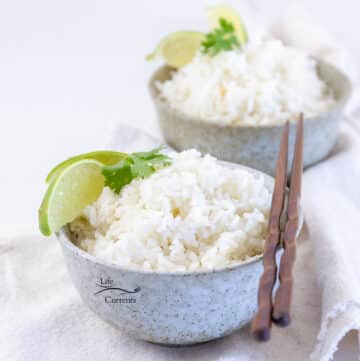 two bowls of rice with lime wedges and cilantro on the top the front bowl has a set of chopsticks on the right.