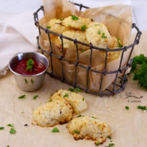 a wire basket with cauliflower appetizers in it with some appetizers in front of the basket and a small cup of dipping sauce.