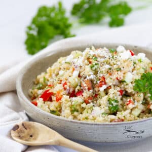 square crop of the side of a bowl filled with quinoa salad and a wooden spoon next to the bowl.