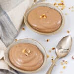 a square crop of two bowls of pudding with a spoon next to them.