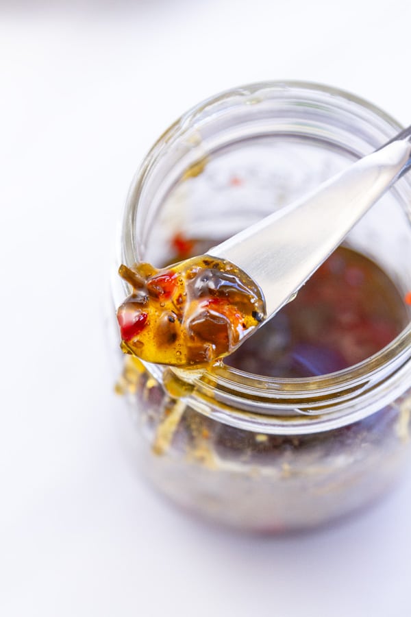 Looking down into a glass mason jar filled with pepper jelly and a spreader on top with jelly on it.