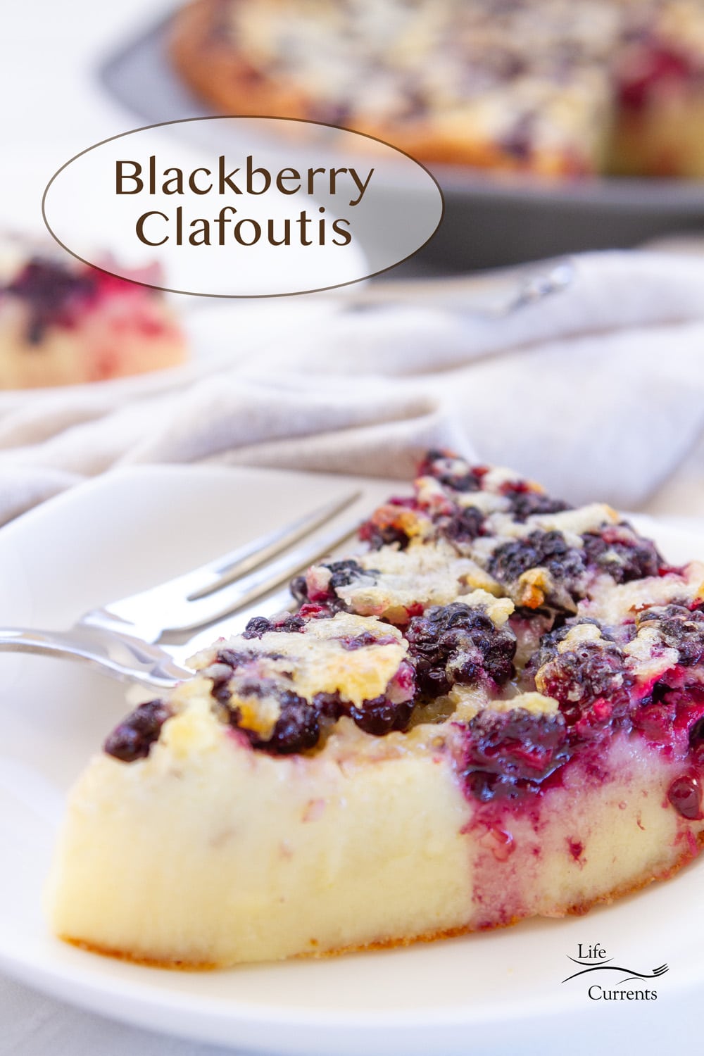 a slice of Blackberry Clafoutis on a white plate with a fork and the whole tart is in the background.