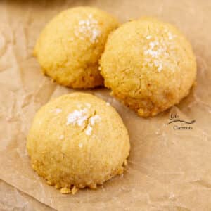 three cookies topped with sea salt on a piece of parchment paper.