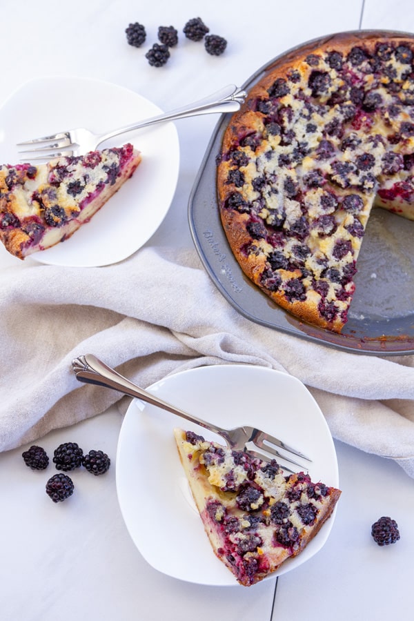 two slices of blackberry clafoutis with the whole pie on the side blackberries scattered around.