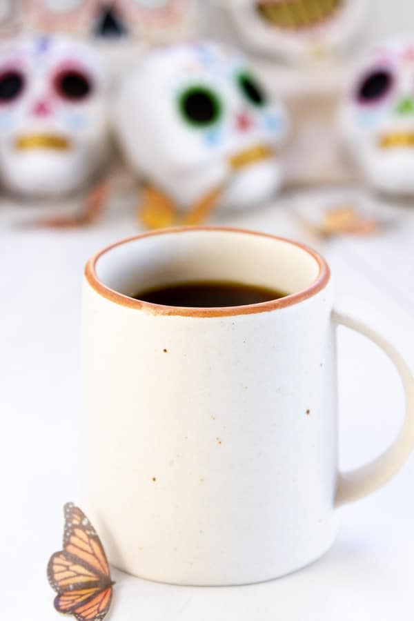 a white mug with day of the dead skulls in the background.