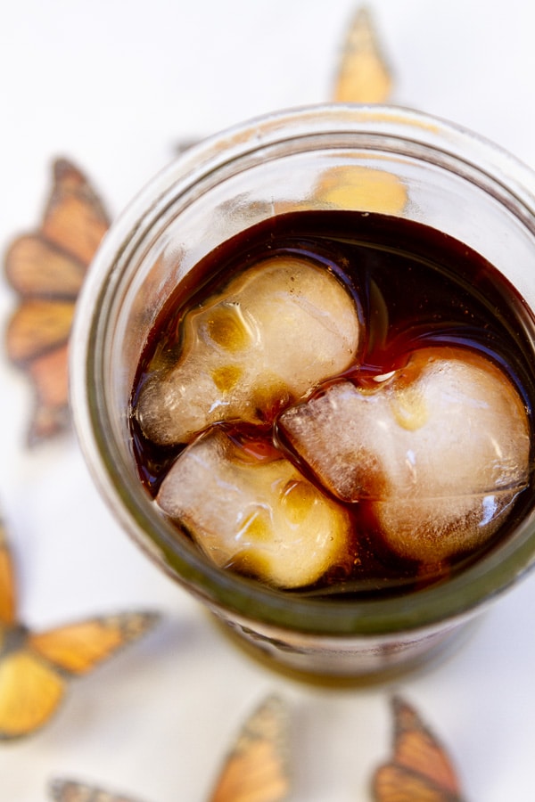 A glass filled with iced coffee and the ice is in the shape of skulls for Day of the Dead.