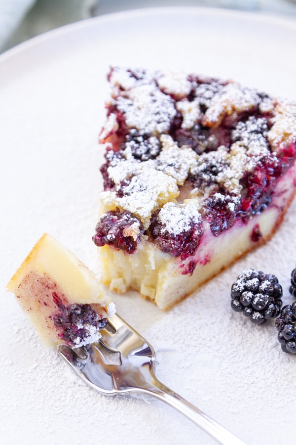 a slice of custard tart dusted with powdered sugar and a bite taken out with a fork.