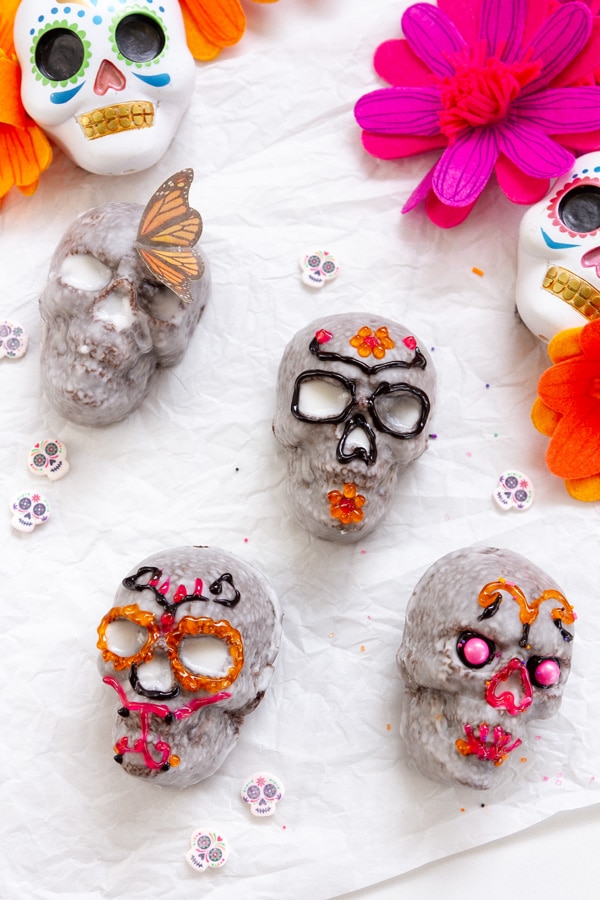 Day of the Dead skulls decorated with icing, sprinkles, and butterflies with pink flowers and skull decorations around them.