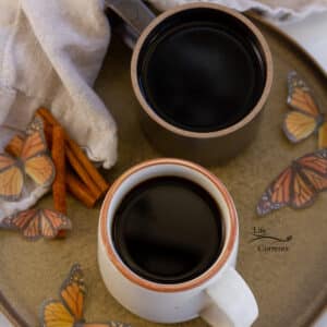 square crop looking down on two cups of coffee on a brown tray with butterflies and a cloth napkin.