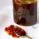 square crop of a jar of pepper jelly with a spoonful of the jelly in front of the jar.