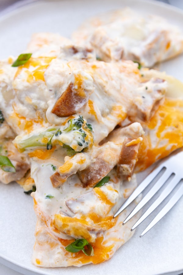 a serving of casserole with pierogi, broccoli, and sausage and a fork on the right of the casserole.