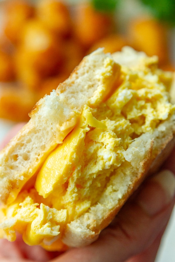 a breakfast sandwich that's been bitten into so you can see the scrambled egg and cheese inside.