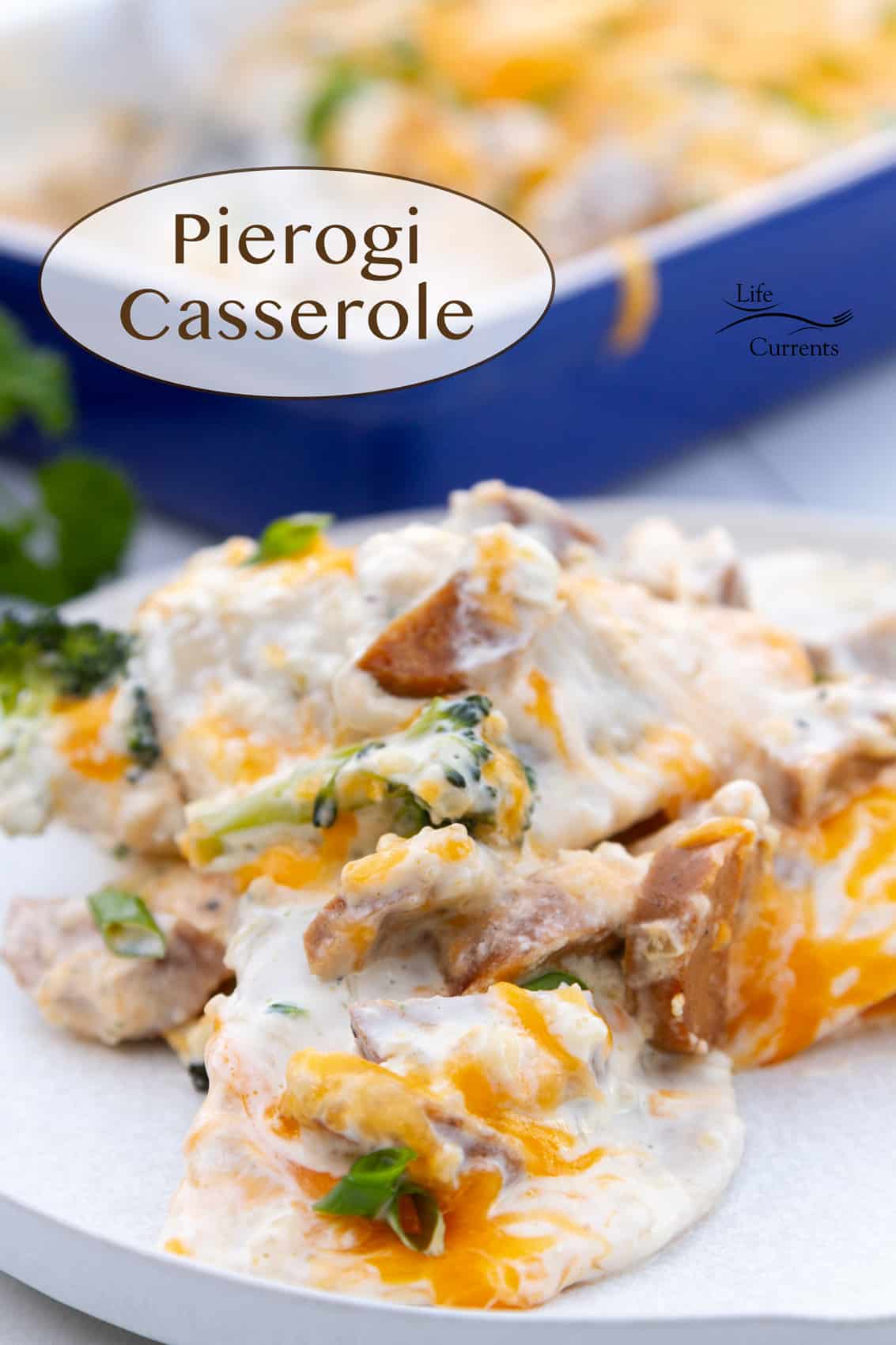 a serving of pierogi casserole on a white plate in front of a blue casserole dish with the rest of the casserole in it.