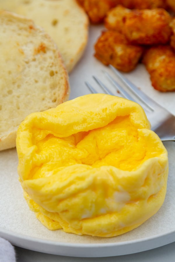 scrambled eggs next to English muffin and tater tots on a plate.