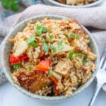 a bowl of cooked rice and vegetables and tofu topped with fresh parsley a fork to the right.