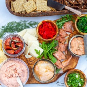 square crop of a tinned fish board with canned fish, vegetables, cheese, crackers.
