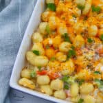 square crop of baked gnocchi in a casserole dish with veggies topped with cheese and herbs, a cloth napkin on the side.