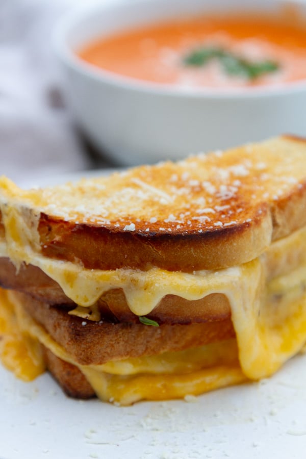 two halves of a sandwich stacked on top of each other in front of a bowl of soup.